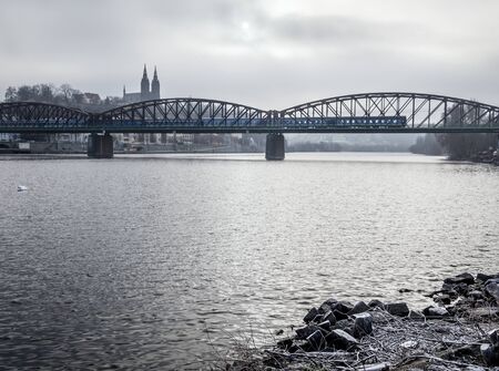 Old railway bridge over the Vltava river in Prague with passing train in winter foggy day.の写真素材
