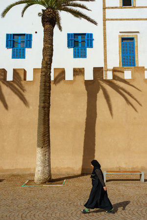 Morocco. Essaouira. A woman wearing a djellaba walking in front of the rampartsのeditorial素材