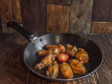 Chicken wings in a frying pan with fresh tomatoの写真素材