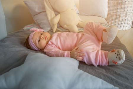 A little baby girl lies on a bed in pink clothes and a bandage on her headの写真素材