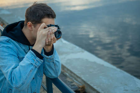 A man in a denim jacket with a vintage film camera at sunset