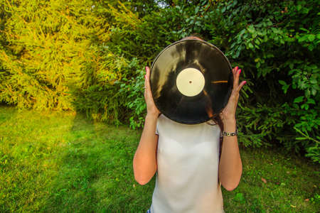 Girl holding a vinyl record in her hands, covering her faceの写真素材