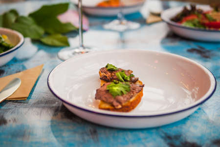 Bruschetta on a white plate in a restaurant. With meat