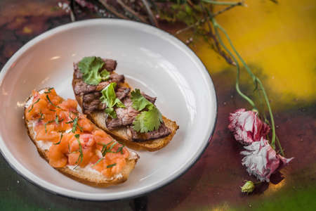 Two bruschetta on a white plate in a restaurant. With fish and meat