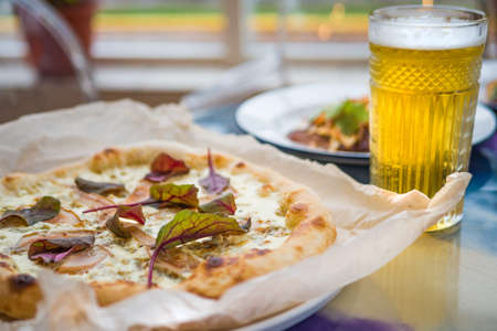 Delicious pizza with cheese and pear with leaves of green on the table in the restaurant and a glass of beerの写真素材