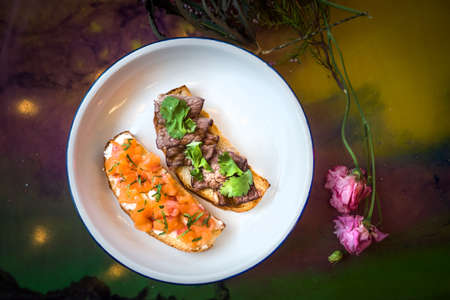 Two bruschetta on a white plate in a restaurant. With fish and meat
