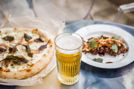 Delicious pizza with cheese and pear with leaves of green on the table in the restaurant and a glass of beerの写真素材