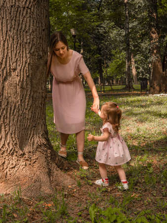 Mom and daughter walk and play in the park. Dressed in dresses. Sunny summer day, weekend in a city park.の写真素材