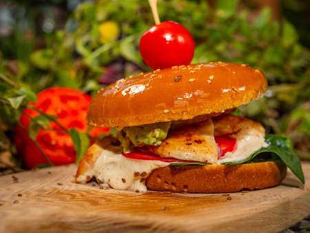 Juicy burger on a wooden board. Hamburger with tomatoes and bacon with white sauce.の写真素材
