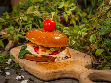 Juicy burger on a wooden board. Hamburger with tomatoes and bacon with white sauce.の写真素材