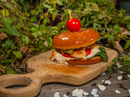 Juicy burger on a wooden board. Hamburger with tomatoes and bacon with white sauce.の写真素材