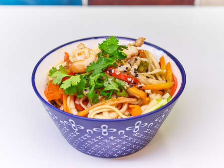 Udon noodles with seafood in a plate on a white surface.の写真素材