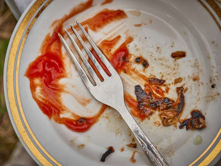 Empty plate with traces of ketchup and meat, fork on top.の写真素材