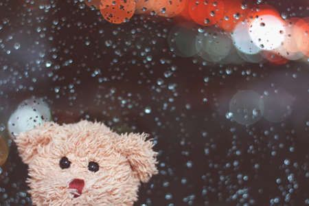 Cute teddy bear with raindrops and lightning on the window in the background, Doll is a lonely feeling when rainingの写真素材