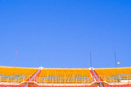 red and yellow Rows of empty seat in football stadium with blue sky backgroundのeditorial素材
