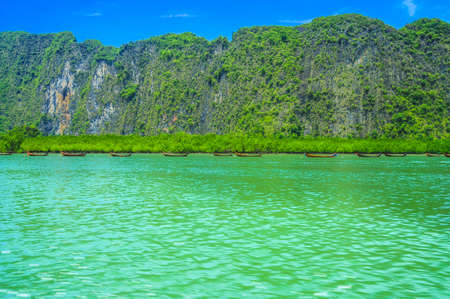 Seaside View of Many Traditional Thai Longtail Boats with Mountain and Blue Sky Background.