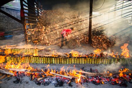 Chonburi, Thailand - April, 10, 2016 : Old woman burns rice roasted in bamboo. sticky rice soaked in coconut milk."Khao Lam" is Thai dessert , coconut milk with sticky rice in bambooのeditorial素材