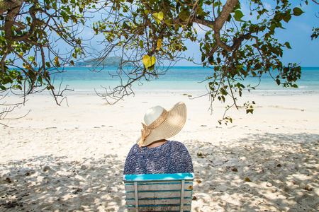 Woman sitting on a beach chair under a tree enjoying a summer day at the beach. Concept on the beachの写真素材