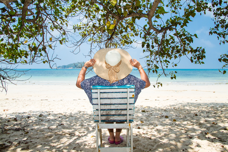 Woman sitting on a beach chair under a tree enjoying a summer day at the beach. Concept on the beachの写真素材