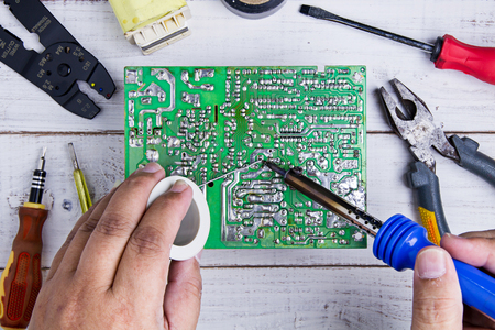 Serviceman soldering circuit board with soldering iron in the service workshop.の写真素材
