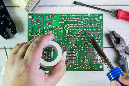 Serviceman soldering circuit board with soldering iron in the service workshop.の写真素材