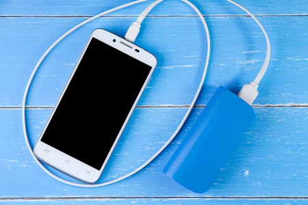 Smart phone and backup battery on the blue wooden backgroundの写真素材