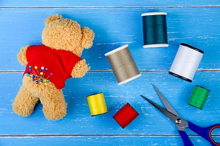 Sewing kit thread and Teddy Bear on the blue wooden background.の写真素材