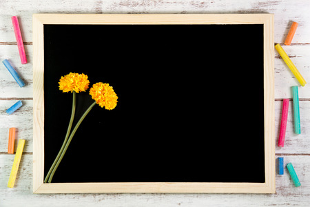 Blank blackboard and Yellow plastic flowers on wooden table.Template mock up for adding your design and leave space beside frame for adding more text.の写真素材