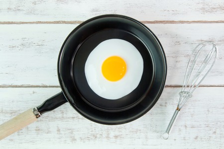 Fried egg in small pan with handle on white wooden board, top viewの写真素材