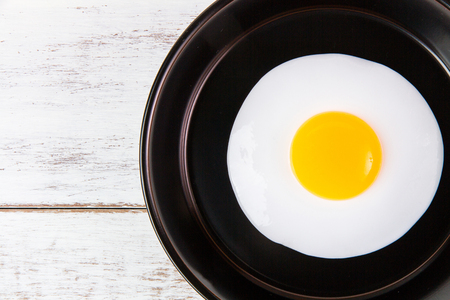 Fried egg in small pan with handle on white wooden board, top viewの写真素材