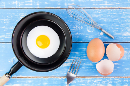 Fried egg in small pan with handle on blue wooden board, top viewの写真素材