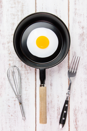 Fried egg in small pan with handle on white wooden board, top viewの写真素材