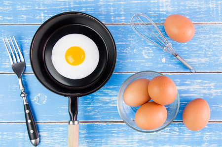 Fried egg in small pan with handle on blue wooden board, top viewの写真素材
