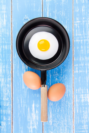 Fried egg in small pan with handle on blue wooden board, top viewの写真素材
