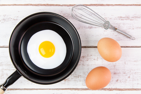 Fried egg in small pan with handle on white wooden board, top viewの写真素材