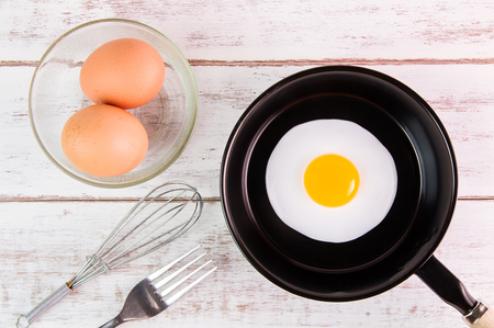 Fried egg in small pan with handle on white wooden board, top viewの写真素材