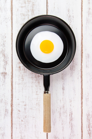 Fried egg in small pan with handle on white wooden board, top viewの写真素材