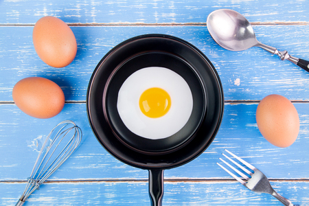 Fried egg in small pan with handle on blue wooden board, top viewの写真素材