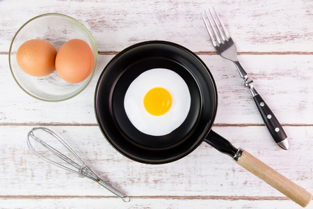 Fried egg in small pan with handle on white wooden board, top viewの写真素材