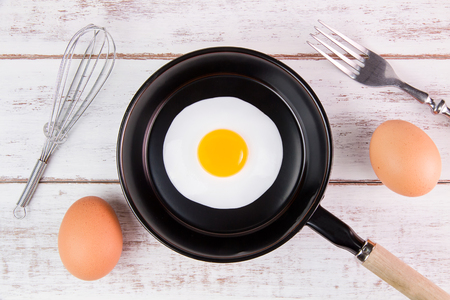 Fried egg in small pan with handle on white wooden board, top viewの写真素材