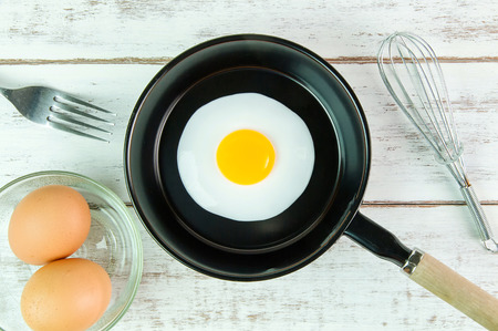 Fried egg in small pan with handle on white wooden board, top viewの写真素材