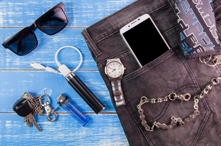 Smart phone, sunglasses, portable battery, jeans, wallet and watch on blue wooden  backgroundの写真素材