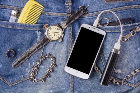 Smartphone, bracelet, portable battery and watch on jeans background.の写真素材
