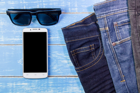 Smart phone, sunglasses,  jeans on blue wooden  background.の写真素材
