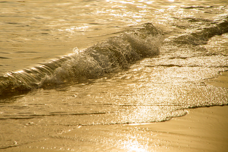 Close up golden sea wave on the sandy beach at sunset.の写真素材