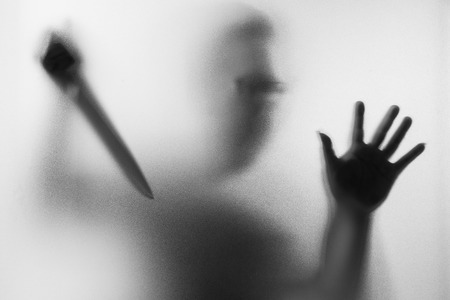 Horror Murderer. Dangerous man behind the frosted glass with a knife on his hand.Halloween background.Black and white pictureの写真素材