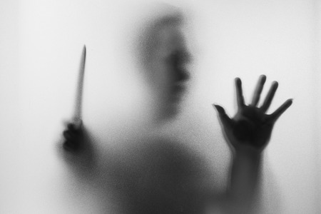Horror Murderer. Dangerous man behind the frosted glass with a knife on his hand.Halloween background.Black and white pictureの写真素材