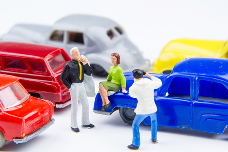 Miniature tiny toys photographer take photos man standing and woman sitting on car bonnet at the public car parking.の写真素材