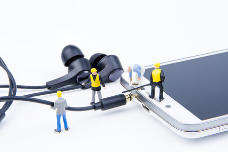Miniature tiny toys team of engineers are doing connected cable 35 mm. earphone jack to the smartphone for listen music.Theme communication technology backgroundの写真素材