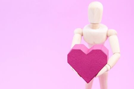 Wooden dummy holding paper box red heart shape on pink background with copy space for your text.Concept Valentine's Day, Day of loveの写真素材